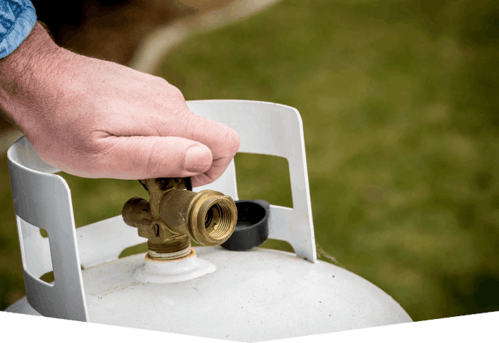 A person opening the valve on an outdoor propane tank.