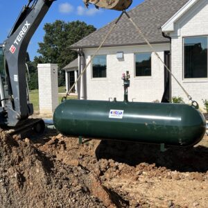 A green tank being lifted into the ground by a crane.