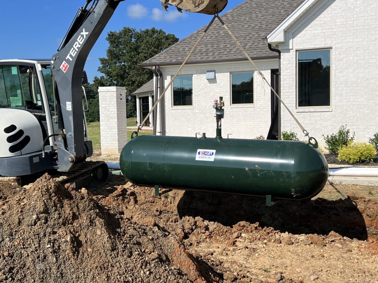 A green tank being lifted into the ground by a crane.